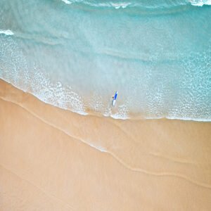 Drone image from above with a surfer walking, holding a surfboard